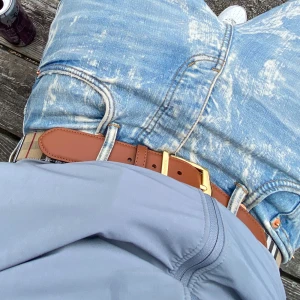 Burberry bälte  - Säljer ett snyggt bälte från Burberry i brunt skinn med klassiskt beige, svart, vitt och rött rutigt tyg på ena sidan. Bältet har ett stort, guldigt spänne med Burberry-logga. Perfekt accessoar för att lyfta din outfit.