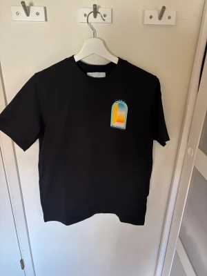 Svart Casa Blanca t-shirt med tryck - Snygg svart t-shirt från Casa Blanca med färgglatt grafiskt tryck fram och stort tryck på ryggen. T-shirten har rund hals och korta ärmar. Perfekt för dig som gillar streetwear och vill sticka ut med cool design.