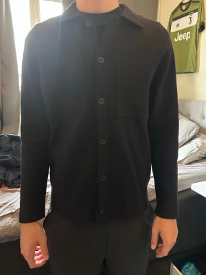 Mörkblå overshirt från Massimo dutti - Stilren blå overshirt med raka linjer och stora bröstfickor. Klassisk krage och knäppning med svarta knappar hela vägen. Tillverkad i ett mjukt, tjockare tyg som ger en clean look. Perfekt att bära öppen eller stängd över en t-shirt.