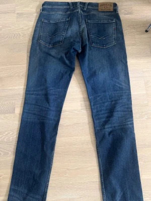 Mörkblå raka jeans från Replay - Snygga mörkblå jeans från Replay ANBASS med raka ben och klassisk femficksmodell. Jeansen har diskreta slitningar framtill och bakfickor med dekorativa sömmar. Tillverkade i mjuk denim som ger en skön passform.