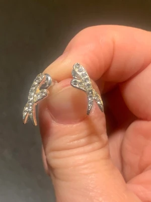 Silvriga örhängen med gnistrande stenar - Säljer ett par silvriga örhängen i form av små grenar eller kvistar, dekorerade med gnistrande stenar. Örhängena är cirka 1,5 cm långa och 0,5 cm breda, har en stilren och modern design. Perfekta för att ge din look lite extra bling.oanvända och i väldigt bra skick 