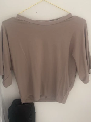 Beige loose topp med trekvartsärm - En enkel och stilren beige topp med lös passform och trekvartsärm. Toppen har en bred halsringning och är tillverkad i ett mjukt material som känns skönt mot huden. Perfekt att matcha med jeans eller kjol för en avslappnad look.