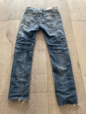 Slim tiger of sweden jeans - Ett par blå jeans med rak passform och slitna detaljer vid bensluten. De har ett litet hål vid högra fickan (se bild) men det smälter in tack vare andra slitningar från fabriken. Materialet är denim i bomull och färgen är tvättad blå. De är i storlek w28 men är mindre än det, skulle säga runt 26/27. Priset är ej hugget i sten!