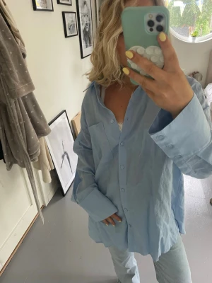 Ljusblå oversized skjorta - Säljer enkelt ny ljusblå oversized skjorta med klassisk krage och stora manschetter. Skjortan har en bröstficka och knäppning framtill. Perfekt för en avslappnad och trendig look.