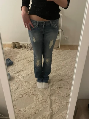 Blå slitna raka jeans - Säljer ett par blå jeans med raka ben och slitna detaljer på låren och knäna. Jeansen har klassisk femficksmodell och normal midja. Perfekta för en avslappnad och trendig look.