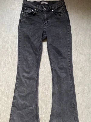 Grå bootcut jeans  - Säljer ett par grå bootcut jeans i klassisk femficksmodell. Jeansen har en snygg tvättad look och utsvängda ben, perfekta för dig som gillar retrostil. Materialet är denim med lite stretch för extra komfort.