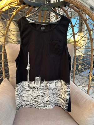 Svart linnetopp med stadsmotiv - Cool svart linnetopp från Seppälä med vit stadssilhuett och liten bröstficka. Skön och luftig modell som passar till många olika outfits.