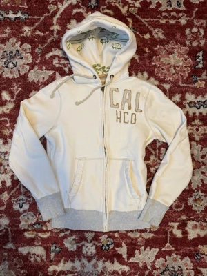 Vit hoodie från Hollister CAL HCO - Hollister Hoodie CAL HCO  • Storlek: S (längd: 63cm axelbredd: 44cm )  • Skick: Använd. Det finns några fläckar (se bilder)  Hör av dig vid funderingar eller om du vill ha mer bilder! 