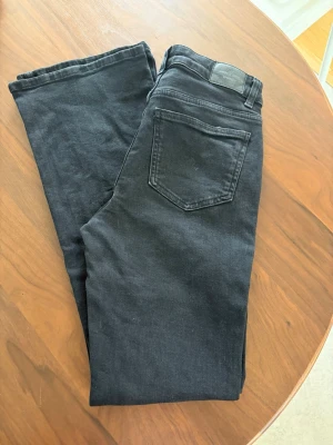 Svarta high waist jeans - Snygga svarta jeans med high waist och klassisk femficksdesign. Jeansen har utsvängda ben och silverfärgade detaljer vid knappar och nitar. Perfekta till alla dina outfits! Mörkare i färgen än vad bilderna visar. Djur finns i hemmet!