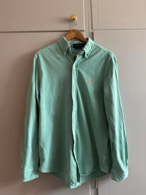 Grön skjorta från Ralph Lauren - Snygg grön skjorta från Ralph Lauren med klassisk button-down krage och broderad logga på bröstet. Skjortan har långa ärmar och knäppning framtill. Perfekt för en stilren look.