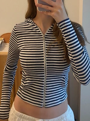 Pull&Bear randig zip-up tröja  - Säljer en snygg långärmad hoodie med dragkedja och huva. Tröjan har marinblå och vita horisontella ränder, figurnär passform och två fickor framtill. Perfekt för en avslappnad och trendig look 🌸 Säljer då jag aldrig har fått användning för den. Storlek xs och nytt skick med prislappen kvar. Kontakta mig om du har några frågor. Pris kan diskuteras 💕✨