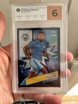 Rodrigo Manchester City samlarkort - Exklusivt samlarkort från 2023-24 Topps med Rodrigo från Manchester City, numrerat 01/50. Kortet är graderat 6 av Professional Card Grading och har svart design med holografiska detaljer. Perfekt för fotbollsfans och samlare.