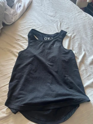 Svart sportig linnetopp - Snygg svart linnetopp med diskreta ränder och sportig design. Perfekt för dig som gillar en enkel och stilren look. Modellen är ärmlös och har rund halsringning. Passar bra till träning eller en avslappnad outfit.