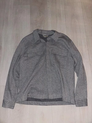 Randig skjorta från Pull&Bear - Snygg långärmad skjorta från Pull&Bear i svartvitt randigt mönster. Skjortan har klassisk krage, två bröstfickor och knäppning framtill. Perfekt för en stilren och avslappnad look.