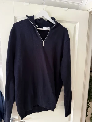 Mörkblå halvzip tröja Selected Homme - Snygg mörkblå stickad tröja från Selected Homme med halvzip och hög krage. Tröjan har långa ärmar, ribbade muddar och är tillverkad i bomull. Perfekt för lager på lager och enkel att matcha med jeans eller chinos.