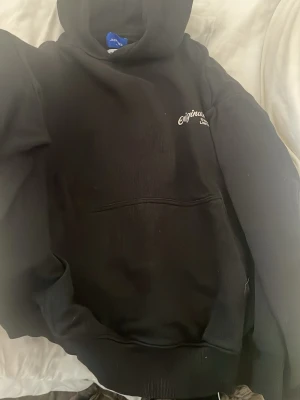 Svart hoodie från Jack & Jones - Säljer en svart hoodie från Jack & Jones Originals med broderad text på bröstet. Klassisk känguruficka framtill och huva med dragsko. Skön och enkel stil som passar till det mesta. Materialet känns mjukt och bekvämt.