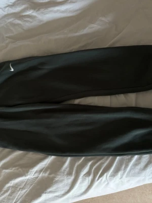 Mörkgröna Nike mjukisbyxor - Jag säljer ett par mörkgröna mjukisbyxor från Nike med den klassiska vita swoosh-loggan på benet. Perfekta för chill dagar eller träning, dem är även väldigt sköna och stilrena. Anledningen är att jag fick dem från ett ex så har ingen användning för dem längre. (Nästan aldrig använda)