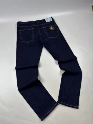 Mörkblå jeans från Stone Island W31 L34 - Snygga mörkblå jeans från Stone Island med raka ben och klassisk femficksmodell. Bakfickan har den ikoniska Stone Island-loggan. Jeansen har kontrastsömmar och är tillverkade i ett slitstarkt denimtyg. Perfekta för en trendig och avslappnad stil.