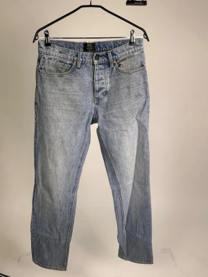 Ljusblå Neuw Jeans - Säljer ett par klassiska ljusblå jeans med rak passform och fem fickor. Jeansen har normal midja, bälteshällor och stängs med knapp och dragkedja. Perfekta för en avslappnad och trendig look.