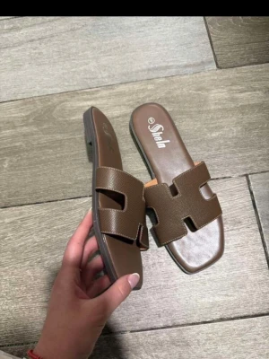 Bruna slip-in sandaler från SheIn - Snygga bruna slip-in sandaler med bred rem i konstläder och trendig utskuren design. Sandalerna har fyrkantig tå och låg sula, perfekta för en chill och stilren look. Passar till både jeans och kjol. Finns i storlek 37 och 38 