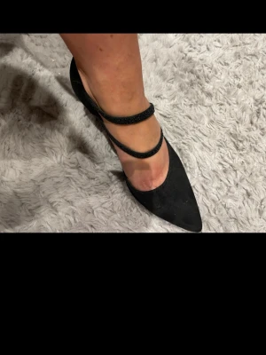 Svarta pumps med dubbla remmar - Snygga svarta pumps med spetsig tå och två tunna remmar över foten. Skorna har en mellanhög klack och ovandelen är i mockaimitation. Perfekta för dig som vill ha en elegant och trendig look.