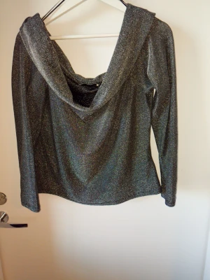Glittrig långärmad topp  - Snygg långärmad topp i glittrigt silvermaterial med en djup öppen rygg och draperad effekt. Perfekt för dig som vill sticka ut och gillar trendiga detaljer. Toppen har en figurnära passform och är superenkel att styla till olika looks.
