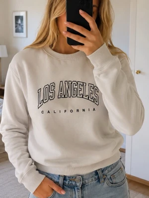 Vit sweatshirt med Los Angeles-tryck - Vit sweatshirt med svart text 'Los Angeles California' på bröstet. Tröjan har rund halsringning, långa ärmar och ribbade muddar vid ärmslut och nederkant. Perfekt för en avslappnad och trendig look. Materialet ser ut att vara mjukt bomullstyg.