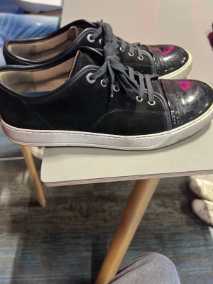 Lanvin cap Toe - Säljer ett par svarta sneakers med snygga lackade tåpartier och vita sulor. Skorna har svarta skosnören och metallfärgade öljetter. Klassisk låg modell som passar till det mesta och ger en clean look.