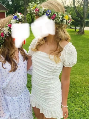 Vit kort klänning med volang - Söt vit kortklänning med puffärmar, volangkant och rynkade detaljer framtill. Klänningen har broderade hålmönster och en feminin, figurnära passform. Perfekt för sommarens alla tillfällen.