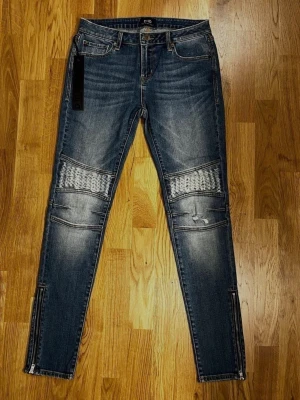Ljusblå jeans från D-ID - Storlek 28 - Ett par snygga och trendiga jeans från D-ID! Jeansen har en snygg ljusblå tvätt och dragkedjor vid bensluten som ger en modern look! Style name: New York. Fit: Moto Zip Skinny. Wash: Blondie. Storlek: 28. Knäpps med knapp och dragkedja. Två framfickor och två bakfickor. Material: 89 % Bomull, 8 % Polyester och 3 % Spandex. Säljs i nytt och oanvänt skick - originallappen sitter kvar! Kika gärna in på mina andra annonser, jag säljer just nu flera klädesplagg! Hör av dig vid frågor och intresse!