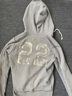 Hollister vintage 2000s zip hoodie - Säljer nu denna sjukt snygga och sällsynta vintage 2000s hoodie från Hollister! Perfekt passform och en både unik och stilren  design med ett ryggtryck😊 Säljs ej längre i butik och är ur en limiterad upplaga och hoodien är därav mycket eftertraktad 🤩Storlek L, måtten ser du bland bilderna. Skriv vid funderingar🤝