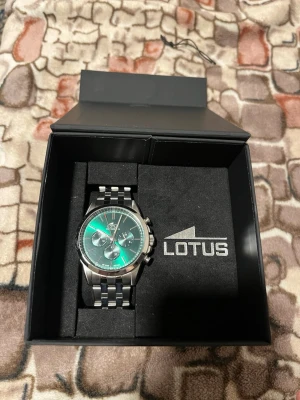 Lotus silverfärgad klocka stållänk - Snygg klocka från Lotus med silverfärgad stållänk och grön urtavla. Klockan kommer med orginal lådan, extra länkar och samt kvitto, Klockan är i god skick eftersom den bara är 4 månader gammal. Kontakta mig vid intresse och frågor.