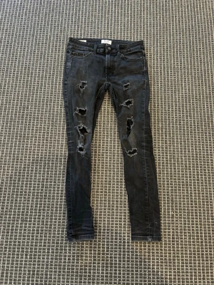 Svarta ripped jeans från Only & Sons - Säljer ett par svarta skinny jeans från Only & Sons med slitna detaljer och stora hål på båda benen. Jeansen har klassisk femficksmodell och knappgylf. Perfekta för dig som gillar en edgy och trendig stil.