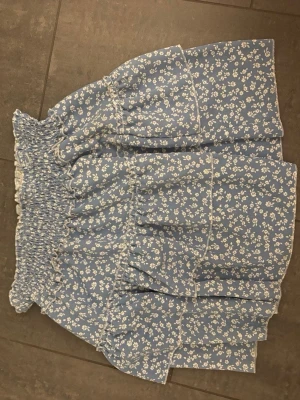 Blå blommig volangkjol från SHEIN - Supersöt blå kjol från SHEIN med vitt blommönster och volangdetaljer. Kjolen har smock i midjan för en bekväm passform och är perfekt för varma dagar. Lätt och luftig känsla, passar perfekt till sommaren.