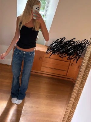 Blå bootcut jeans med låg midja - Säljer ett par blå bootcut jeans med låg midja och klassisk femficksdesign. Jeansen har en avslappnad passform och är tillverkade i denim med lätt slitning. Perfekta för en trendig och avslappnad look💕💕