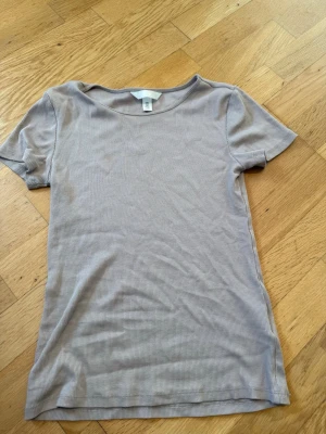 Beige ribbad t-shirt - En enkel och stilren beige t-shirt med ribbad struktur och korta ärmar. Perfekt basplagg med rund halsringning. 