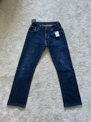 Mörkblåa Blåa Nudie Selvedge Jeans Average Joe 2016 Storlek W30 L32 - Mycket fina Nudie Jeans i blå färg. | Jeansen är i mycket bra skick och sparsamt använda. |  Äkta som allt annat jag säljer! ✅ |  Storlek: W30 L32 (Blivit omsydda i midjan, var tidigare W33)  | Skick: Mycket Bra Skick (SE SISTA BILDER) | Färg: Blå | Märke: Nudie | Modell: Jeans |   Hör gärna av dig vid frågor så svarar jag så fort jag kan! 😁 |  (SKU - 212)