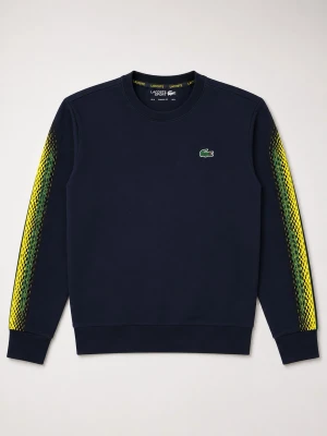 Mörkblå sweatshirt från Lacoste - Snygg mörkblå sweatshirt från Lacoste med det klassiska krokodilmärket på bröstet. Ärmarna har coola gula och gröna grafiska detaljer längs sidorna. Tröjan har rund halsringning och ribbade muddar. Perfekt för dig som vill ha en sportig och trendig look.                                                 ordepris: 800kr 