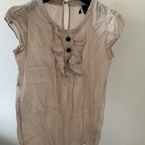 Beige Blus - En vacker beige kortärmad blus med svarta knappdetaljer