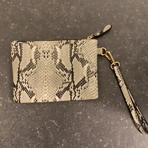 Ormskinnsväska i grått, svart och vitt - Ormskinnsväska i grått, svart och vitt, guldig dragkedja, bandet kommer inte med, säljer pga att den inte kommer till användning, endast använd en gång, sååå fin till våren, 100kr