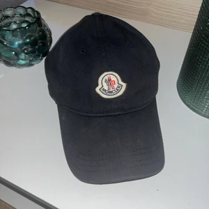 Moncler keps - Keps från Moncler. Trendig keps i en minimalistisk design. Broderad logotyp mitt fram. Justerbar passform med spänne baktill. Struktur i skärmen. Knappt använd. Mycket bra skick. 
