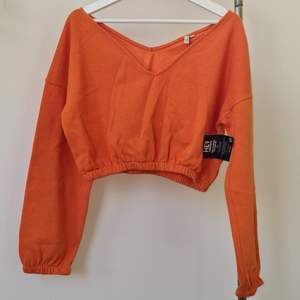 En orange crop-sweatshirt med puffärmar och v-ringad hals. Oanvänd med prislapp kvar! Köparen står för fraktenen.