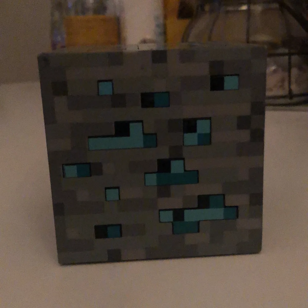 Detta är en Minecraft baserad nattlampa. Den lyser i blått (batterierna i den var döda dock, så kan inte visa). Påtal om det, så ingår inte batterier. För att sätta på den, knackar man lätt på den. Destu mer man knackar, destu mer lyser den :). Övrigt.