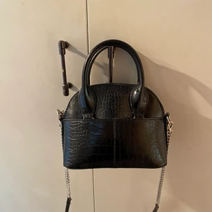 Svart miniväska  - Svart miniväska från Zara med krokodilmönster. Väskan har ett band som man kan ta av. Säljer den då den inte kommit till användning så den är i väldigt fint skick.