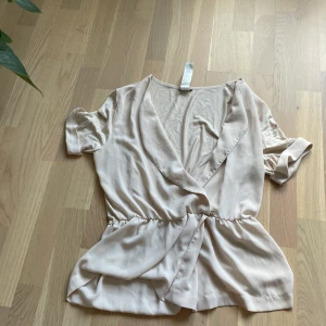 Kortärmad blus med djup vringning - Kortärmad ljus beige blus med djup vringning. Storlek L