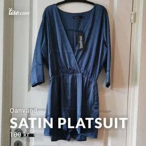 Jumpsuit - Oanvänd satin playsuit i en mörkblå färg från Boohoo. Fin urringning som även kan stängas igen med en säkerhetsnål. Markerar midjan, passar även med ett bläte. Storlek 36 men stor i storleken, passar mer en 38a. Kanske en 40, är osäker. 