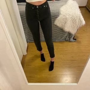 Mom jeans Storlek 34 - Snygga mom jeans från NA-KD. Byxorna sitter som en smäck över rumpan och är lite vidare längs benen och slutar ganska kort. De är i en lite urtvättad svart färg lite mot gråa hållet och knäpps med knappgylf. Jag är 1,73 och bär oftast sorlek 36/small. 
