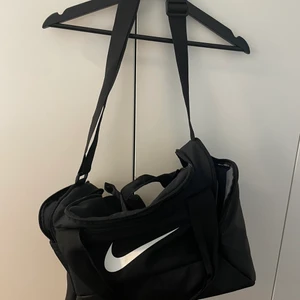 Nike Performance UNISEX - Sportväska - Svart/Vit Sportväska från Nike. Nyskick.                                                  Sport: Fitness Stängning: Dragkedja Fack: Rymligt innerfack Indelning: Framficka                                                      Höjd: 25 cm i storlek One Size Längd: 38 cm i storlek One Size Vidd: 23 cm i storlek One Size Handtag: 22 cm i storlek One Size