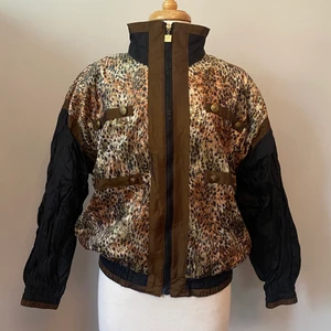 Retro vindjacka - Asball retro vindjacka med sammetsliknande leopardmönstrat material över det klassiska vindjacke-materialet. Fina gulddetaljer i form av små prickar och stjärnor över leopardmönstret. Tippar på storlek L men sitter snyggt oversize på mig som är en storlek S. 