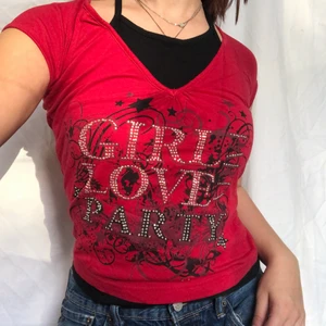Röd topp med coolt tryck - Rött linne med inbyggd svart halterneck! Smyckad med rhinestones och svart tryck. Visas på en s men passar både större och mindre beroende på önskad passform. Gott defetfritt skick. Köpare står för 48kr frakt. 
